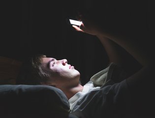 A young male stares at their phone in bed.