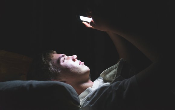 A young male stares at their phone in bed.
