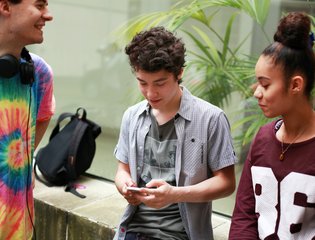 A group of young people mingle while on their phones.