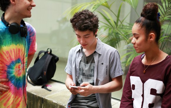 A group of young people mingle while on their phones.