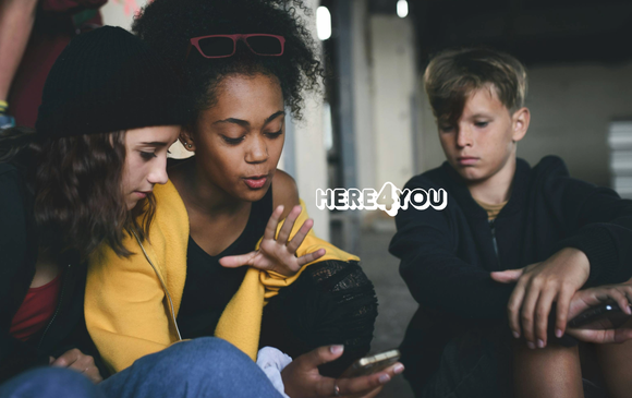 A group of young people look at a phone.