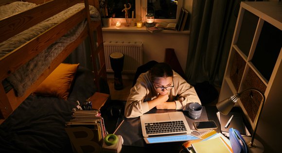 A young person stares at their laptop in their dorm room.