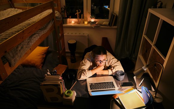 A young person stares at their laptop in their dorm room.