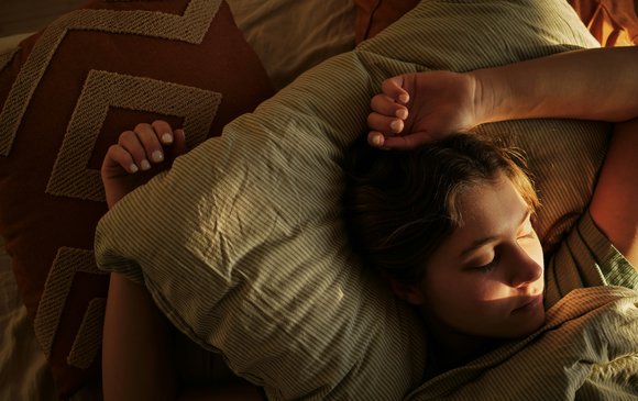 A young person sits in bed with the sun reflecting on them.