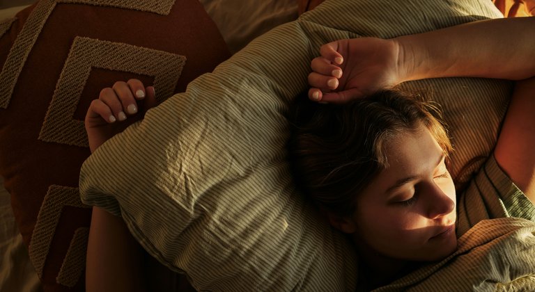 A young person sits in bed with the sun reflecting on them.