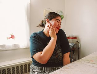 A young female smiles as she touches her face.